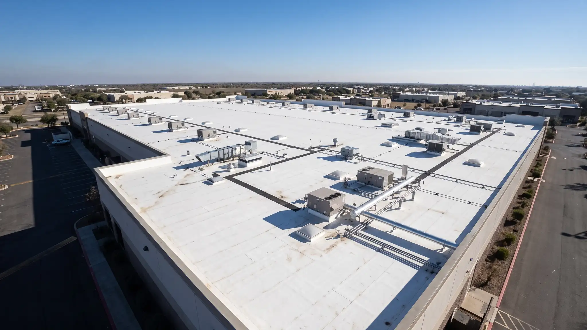 A large commercial building with a clean white TPO flat roof with rooftop units and a clear blue sky